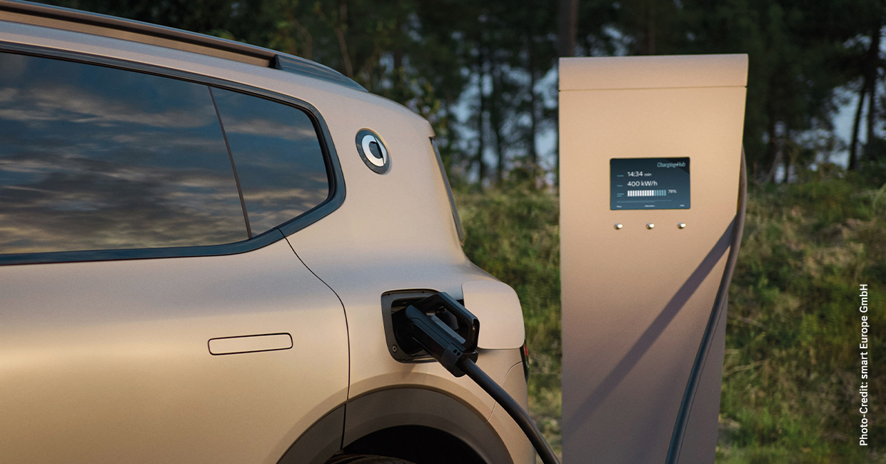 Seitliche Aufnahme eines mattgoldenen SUVs, der gerade an einer Schnellladesäule mithilfe eines Ladekabels geladen wird.